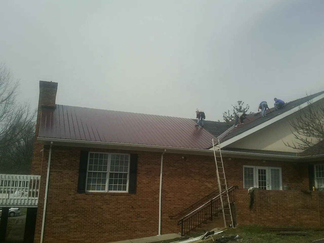 Crew setting red metal roofing panels on a brick home in Garland